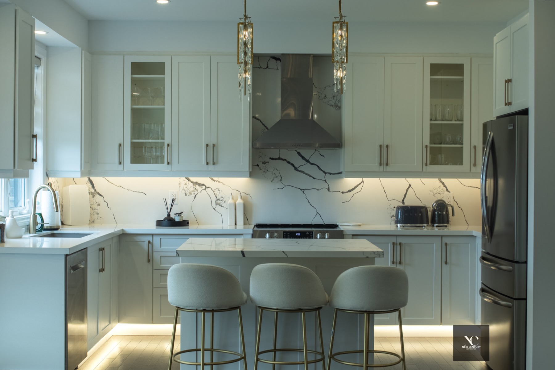 White shaker kitchen with marble backsplash, brass pendants and lit toe kicks